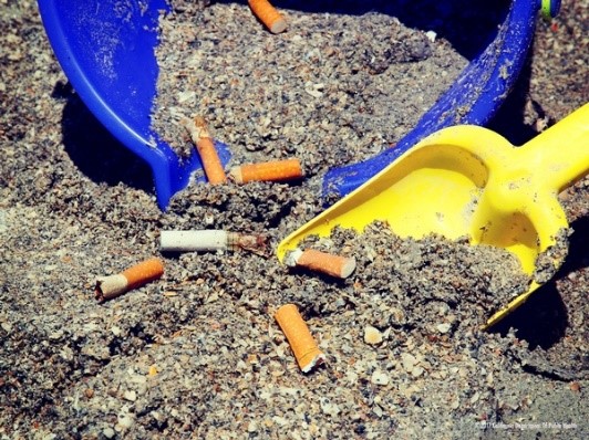 Cigarette butts in sand being scooped up with sand toys