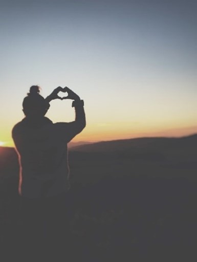 Picture of woman overlooking hills making a heart with hands